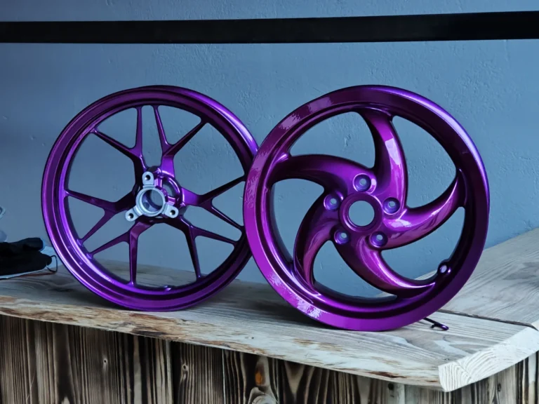 Zwei violett beschichtete Motorradfelgen auf einer Holzfläche